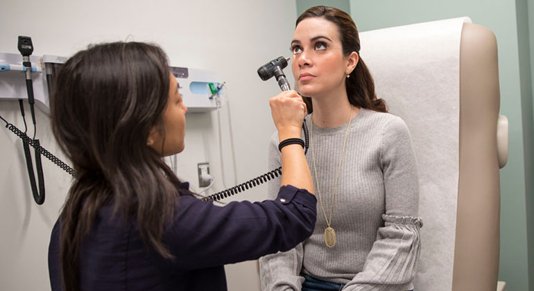 Female doctor examining female woman’s eyes with light